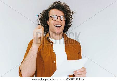 Happy Handsome Saleman With Curly Hair, Writes On Paper For New Plans For Business Posing Over White