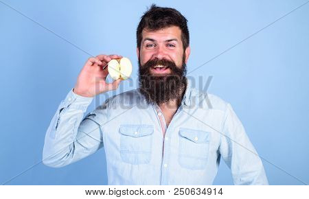 Man Bearded Smiling Holds Apple Blue Background. Healthcare Dieting Vitamin Nutrition. Half Of Apple