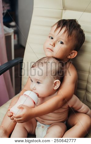 Brother Feeding Little Sister With Milk Or Cereal With A Bottle