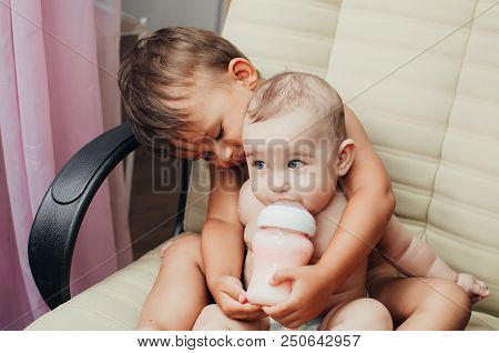Brother Feeding Little Sister With Milk Or Cereal With A Bottle