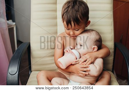Brother Feeding Little Sister With Milk Or Cereal With A Bottle