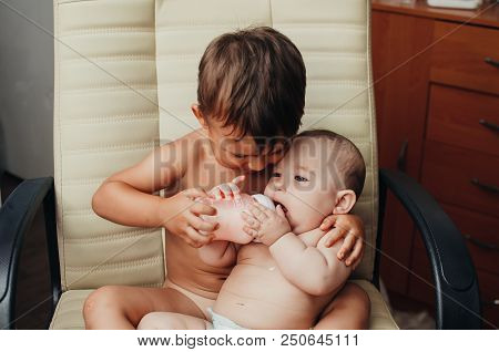 Brother Feeding Little Sister With Milk Or Cereal With A Bottle