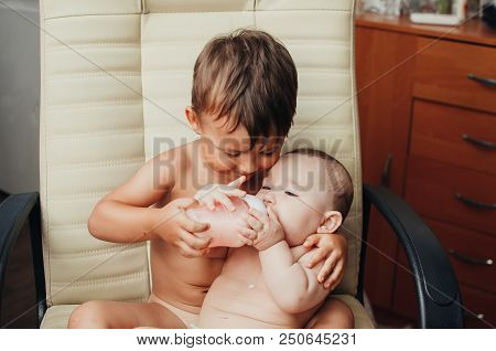 Brother Feeding Little Sister With Milk Or Cereal With A Bottle