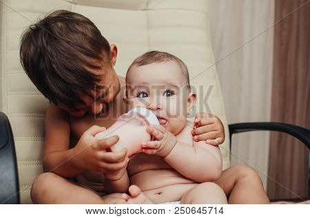 Brother Feeding Little Sister With Milk Or Cereal With A Bottle