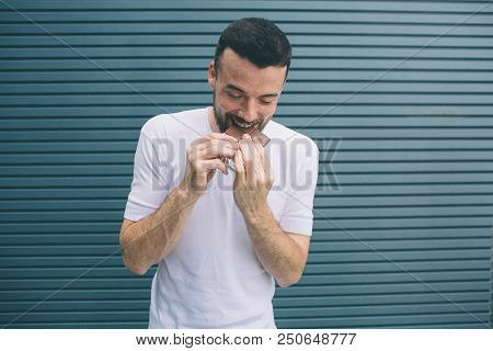 Brunette Man Is Looking Down And Biting Piece Of Chocolate. He Holds It With Both Hands. Isolated On