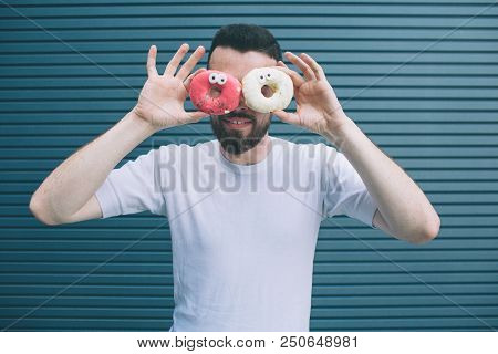 Funny Picture Of Man Holding Two Colorful Donuts Around His Eyes. He Is Looking On Camera And Smilin
