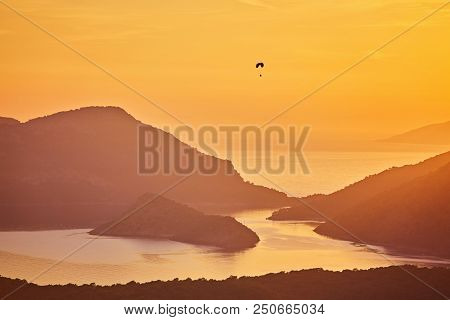Silhouette Of Powered Paraglider Soaring Flight Over The Sea Against Marvellous Orange Sunset Sky. P