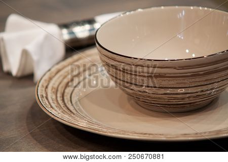 Brown Porcelain Plate, A Bowl And A White Napkin On A Wooden Table