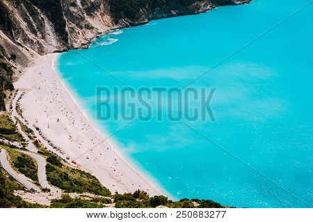 Famous Myrtos Beach With Blue Water On Sunny Day. Tourists On The Sandy Beach, Kefalonia, Greece.