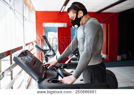 Man Resting Before The Next Race, Doing Sports, In A Training Mask For Breathing On The Treadmill, M