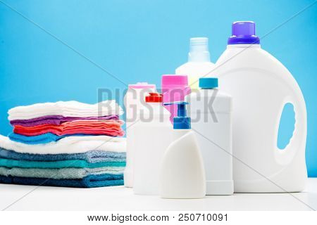 Photo of different bottles of cleaning products and colored towels on table isolated on blue background