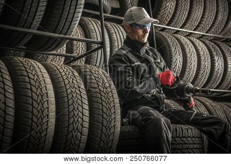 Car Tires Sales And Repair. Service Worker With Power Tool Between New And Used Tires. Automotive Th