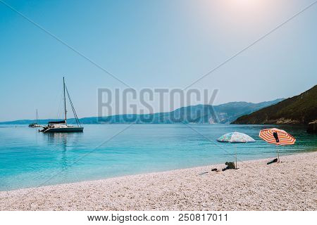 Idyllic White Beach With Umbrellas On Lazy Summer Day. Sailing Boat On Calm Crystal Clear Water.