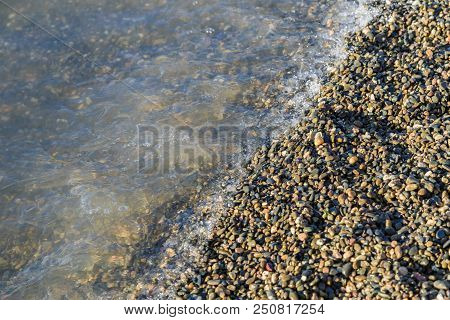 Pebbles On The Beach Pebbles On The Sea Shore And Waves Of Water Illuminated By The Rays Of The Sun