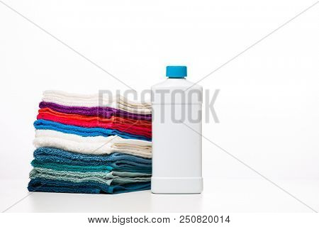 Photo of one bottle of detergent and multi-colored towels on clean white background
