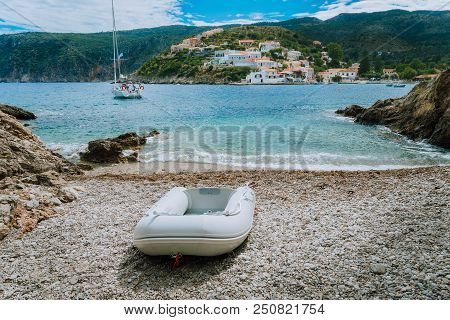 A Dinghy On Small Hidden Beach In Assos Village. White Yacht In Assos Bay. Kefalonia Greece.