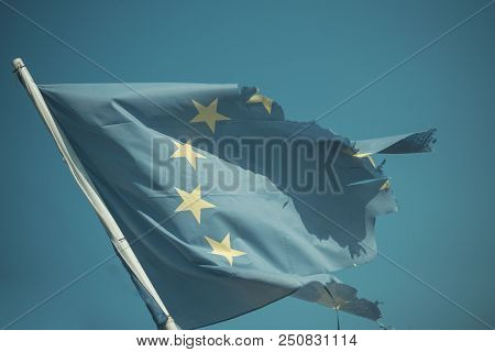 Euro Skepticism Concept. Torn Eu Flag Wave On Blue Sky. European Union Flag With Twelve Stars On Sun