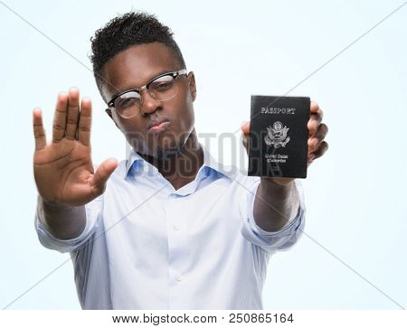 Young african american man holding passport of united states of america with open hand doing stop sign with serious and confident expression, defense gesture
