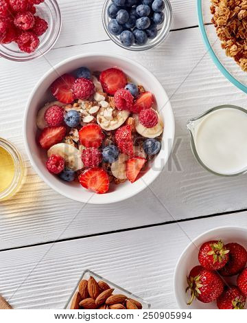 White ceramic bowl with natural organic berries, fruits, nuts, milk, muesli on wthite wooden background.