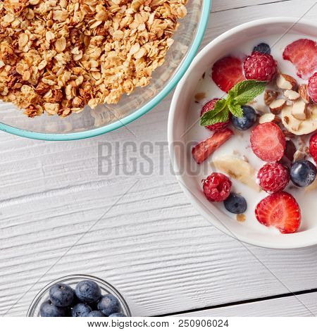 A ready breakfast of natural organic ingredients - granola, berries, nuts, honey, milk for the preparation of natural healthy food on white table.
