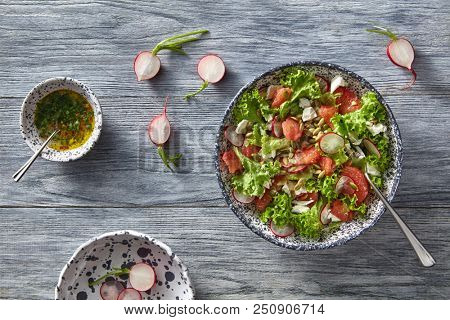 Fresh spring salad with radish, tomatoes, greens in ceramic bowl on gray wooden table. Flat lay.