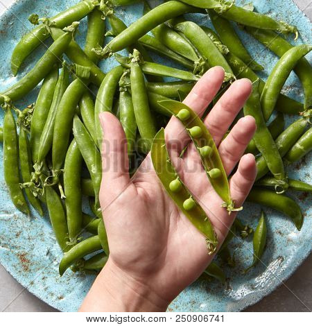 Pear sticks on a woman hand and organic freshly picked green vegetables for preparing vegetarian salad on blue ceramic plate. Flat lay.