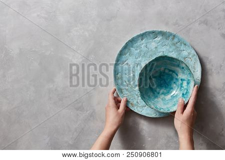 Vintage painted glazed plates dishes on gray concrete table with free space ror text. Girl hold handcraft bowl in her hand. .