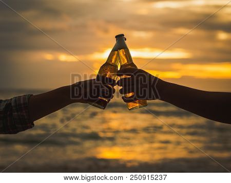 Couple Hands Holding Beer Bottles And Clanging On The Sunset Beach. Party, Holiday, Summer, Friendsh