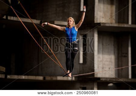 Female Equilibrist Balancing With Arms Raised On The Slackline Rope On The Background Of Section Of 