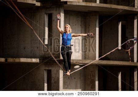 Female Equilibrist Standing With One Arm Raised And Other To The Right On The Slackline On The Backg