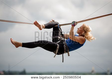 Attractive Female Equilibrist Hanging On The Slackline Rope Upside Down On The Background Of Clear S