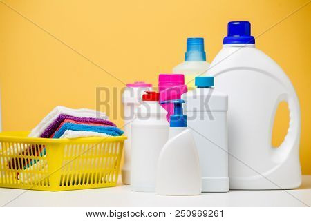 Photo of several bottles of cleaning products and multi-colored towels in basket isolated on orange background