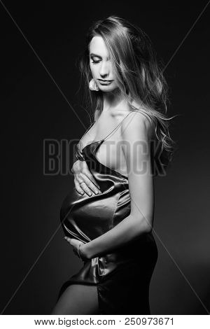 Monochrome Portrait Of Gorgeous And Beautiful Pregnant Woman In Sexy Silk Dress, Embracing Belly. Fa
