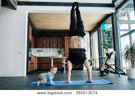 Man Performing A Hand Stand Next To His Jolly Infant Baby