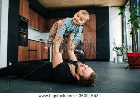 Happy Loving Father Lying On A Floor, Lifting His Baby In The Air