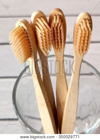 A Family Set Of Four Wooden Toothbrushes In A Glass On White Wooden Background