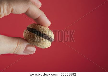 Female Hand Holds A Cookie Called Bacio Di Dama On A Red Background