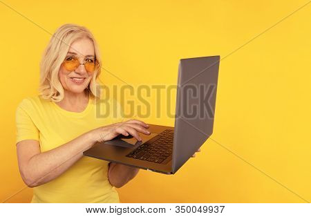 Portrait Of Happy Exited Abult Lady With Laptop Isolated Over The Yellow Studio.