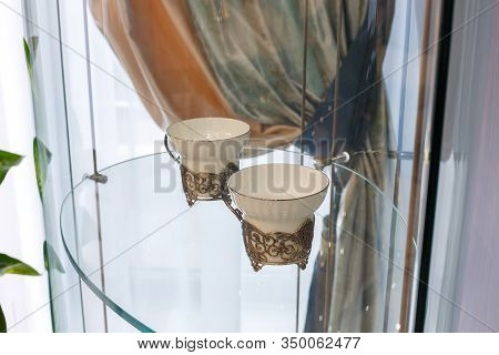 Cups on the glass shelf of the cabinet. Beautiful ornament on the background of the curtains. The interior of the living room.