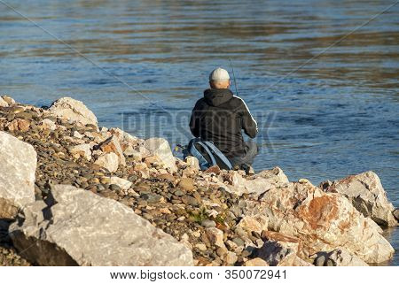 A Fisherman With A Fishing Rod Catches Fish From A Rocky Shore On A Sunny Autumn Day
