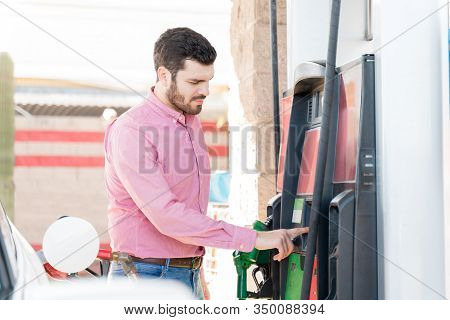 Hispanic Young Adult Man Operating Fuel Pump Machine At Self-service Gas Station