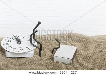 Figurines Of Man Made From Carpentry Nails. They Are Sitting On The Watch Dial, Next To Each Other.