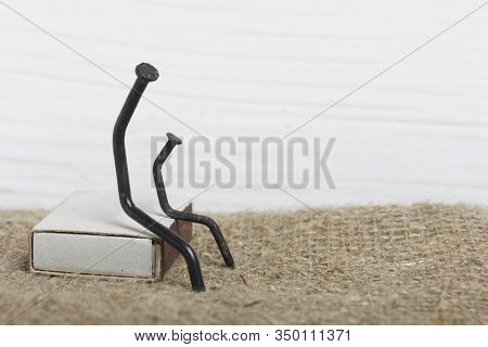 Figurines Of Man Made Of Carpentry Nails. Sit On A Box Of Matches, Next To Each Other.