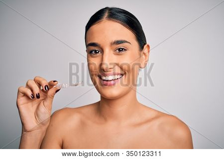 Young beautiful brunette woman holding dental aligner orthodontic to teeth corretion with a happy face standing and smiling with a confident smile showing teeth