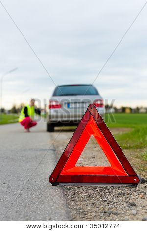 Mladá žena s výstražný trojúhelník na ulici po poruše auta