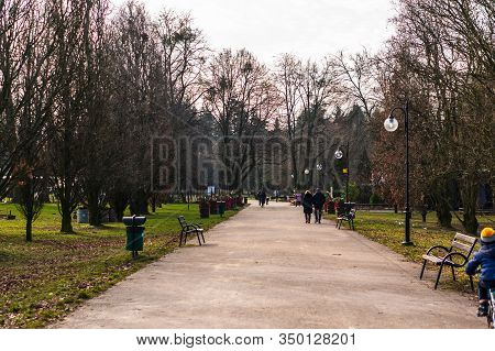 Poznan, Poland - February 9, 2020: Broad Footpath With Benches And Walking People Along Green Grass 
