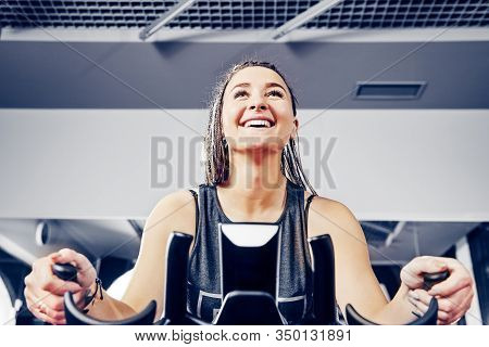 A Cheerful Young Girl Working Out On A Bike Simulator At A Fitness Center. Healthy Lifestyle. Fitnes