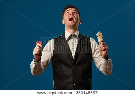 Noob In Poker, In Black Vest And White Shirt. Holding Two Red Chips And Aces. Posing Against Blue Ba