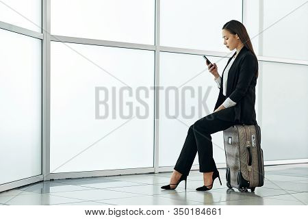 Young Asian Business Woman In Airport With Baggage Trolley Bag, Talking On The Phone And Smiling.