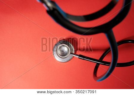 black stethoscope on a red background top view with copy space.